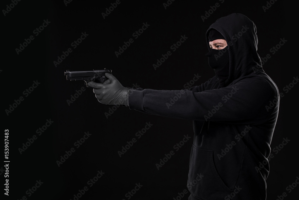 The robber in a mask with a gun pointed to the side on a black background The robber in a mask with a gun pointed to the side on a black background