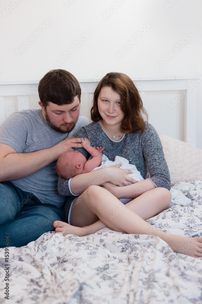 Young parents cradling their newborn baby girl, resting on white bed. Natural, lifestyle image with shallow depth of field. Young parents cradling their newborn baby girl, resting on white bed. Natural, lifestyle image with shallow depth of field.