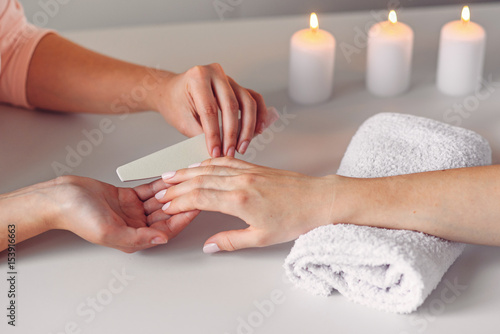 Spa salon. Beautiful woman hands having nail filing with nail file by manicurist. Cosmetic procedure, manicure on female hand.