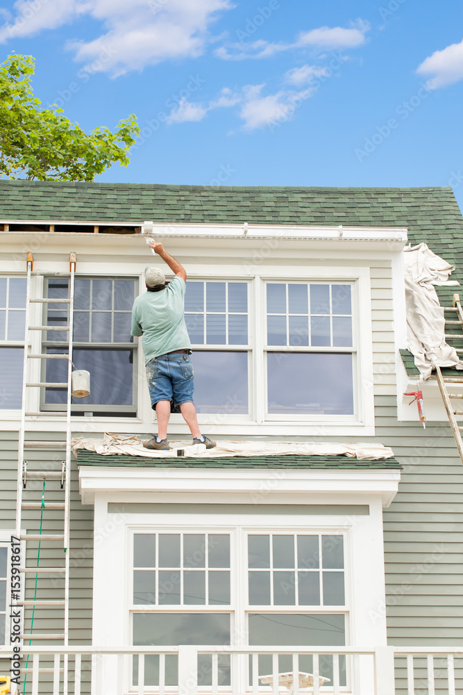 House painter with a tall ladder brushes paint onto the trim on a house