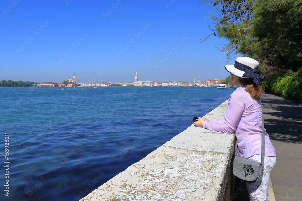 Young woman in a hat standing on the bridge and looking on the city of Venice