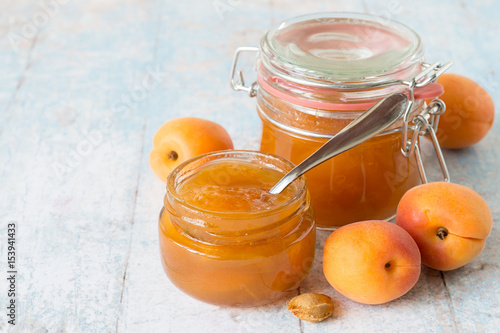  Freshly cooked dessert. Ripe apricots and two jars of jam on a light wooden background.