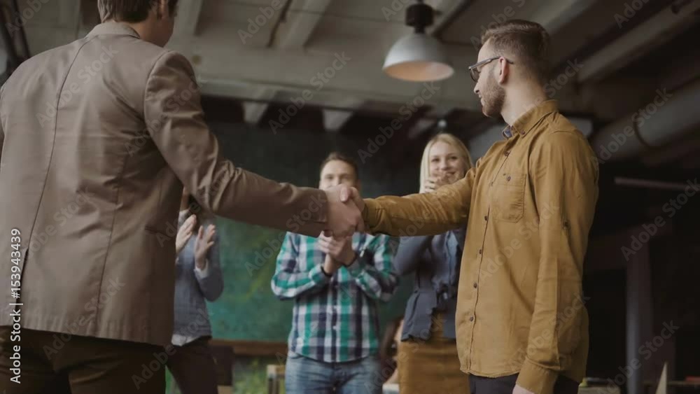 Two partners, businessman shake hands. Group of people clapping on a background. Manager congratulates trainee promotion Two partners, businessman shake hands. Group of people clapping on a background. Manager congratulates trainee promotion