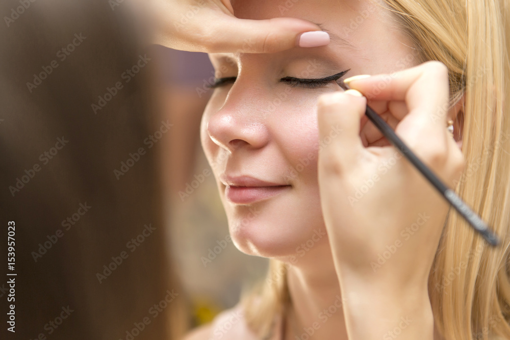 Brunette make up artist woman applying make up for a blonde bride in her wedding day. Making eyes shadows make up