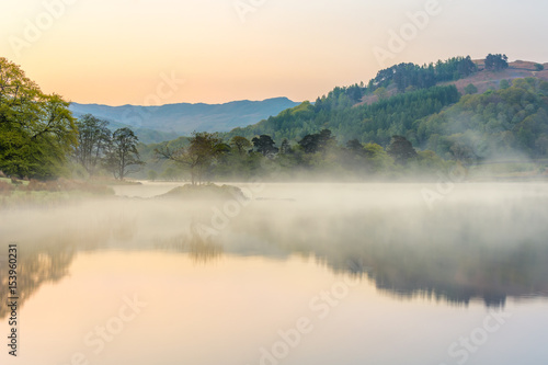 Misty spring morning at Rydal Water in the English Lake District with calm reflections in water.