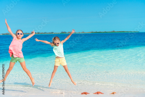 Adorable little girls having fun on the beach full of starfish on the sand