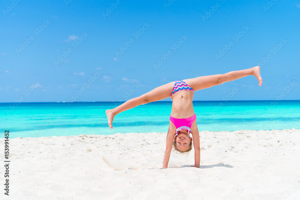 Active little girl at beach having a lot of fun. Sporty kid makes the wheel on the seashore Active little girl at beach having a lot of fun. Sporty kid makes the wheel on the seashore