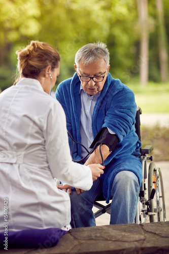 assessment of blood pressure elderly man in wheelchair.