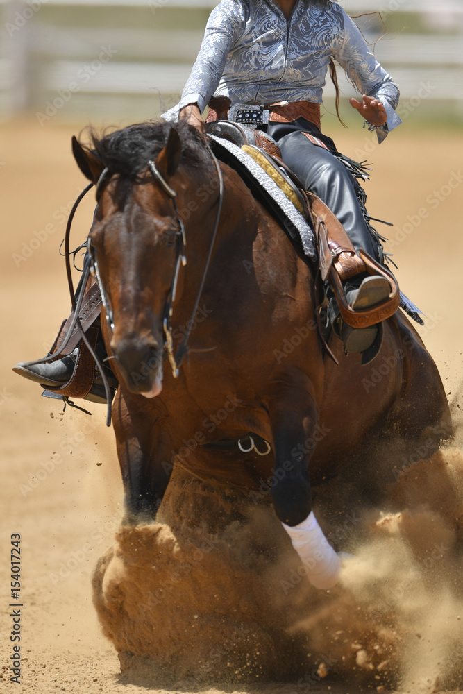 Obraz premium The front view of a rider in cowboy chaps and boots sliding the horse in the sand