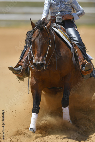 The front view of a rider in cowboy chaps and boots sliding the horse in the sand