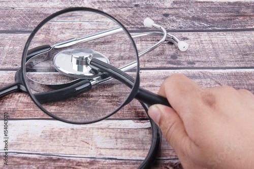 Hand Holding Stethoscope With Magnifying Glass On Wooden Background.