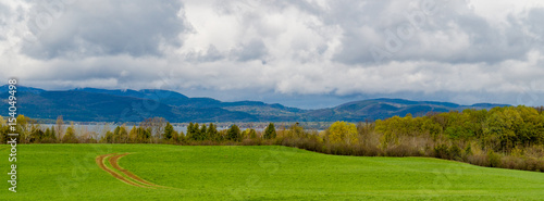 banner picture of farm meadow with tractor tracks curving across field looking to Lake Champlain, Vermont , across to mountains in New York State © vermontalm