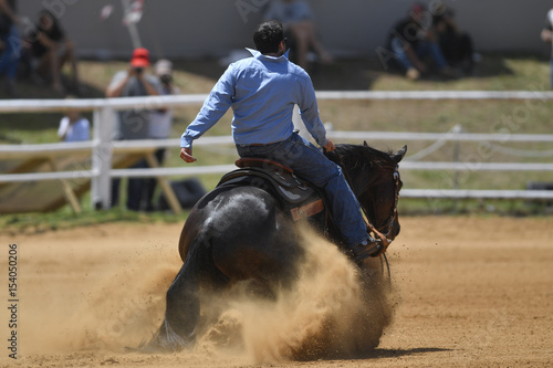 The rear view of a rider in cowboy chaps and boots sliding the horse in the sand