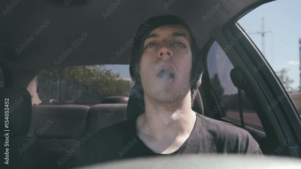 Man vaper makes smoke with electronic cigarette sitting in car in slowmotion. Man vaper makes smoke with electronic cigarette sitting in car in slowmotion.
