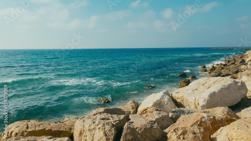 WIDE Handheld daytime shot of calm sea, waves splashing over the rocky shore. 4K color graded footage photo