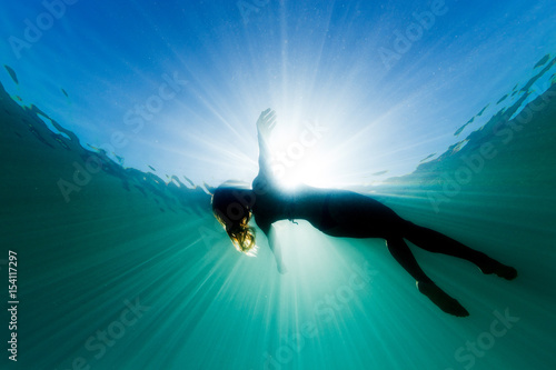 A beautiful woman floats on her back in the ocean as she is surrounded be bright ethereal light and sun rays.
