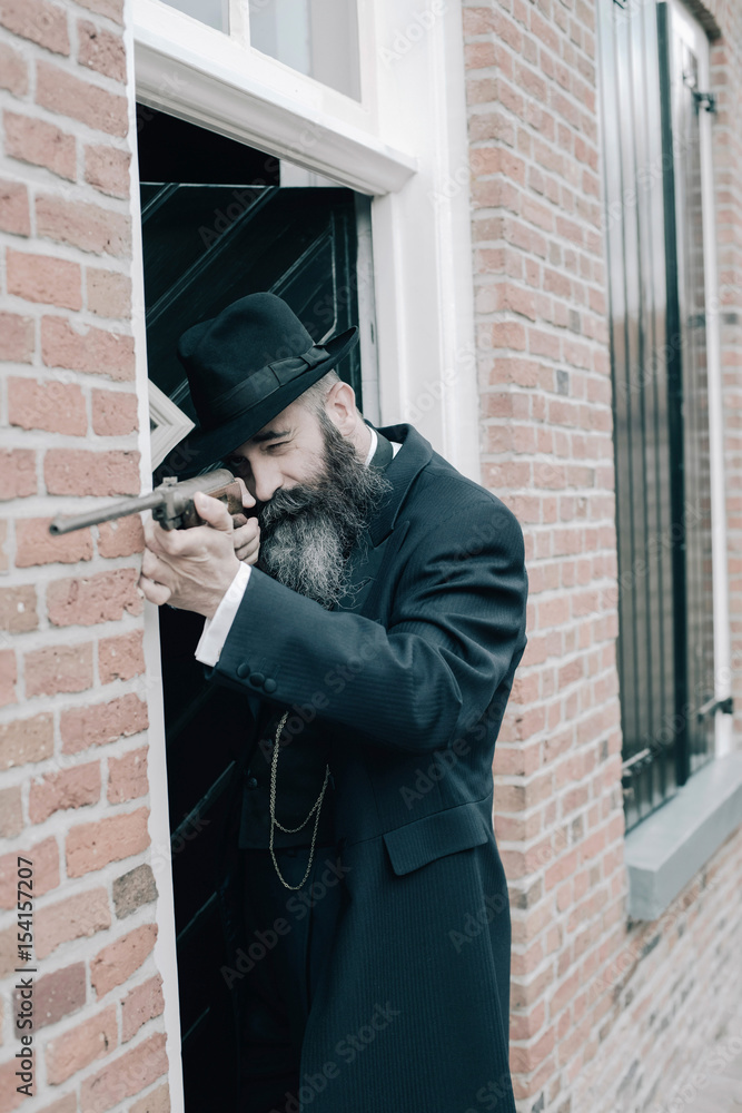 Long bearded man shooting with rifle along wall near front door.