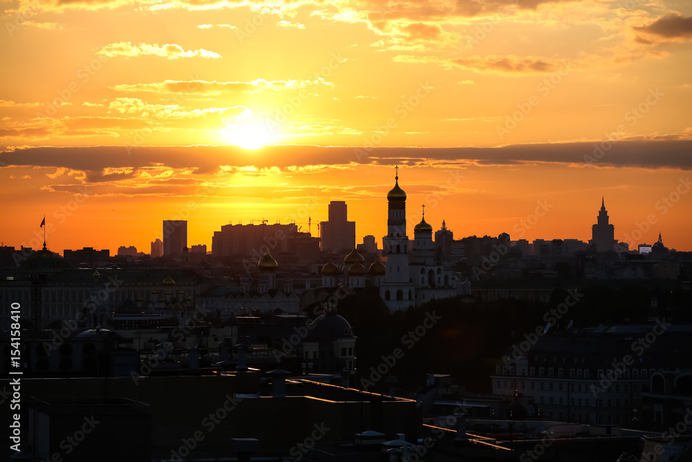 The sun sets over Moscow, silhouettes of houses and churches against the sky.