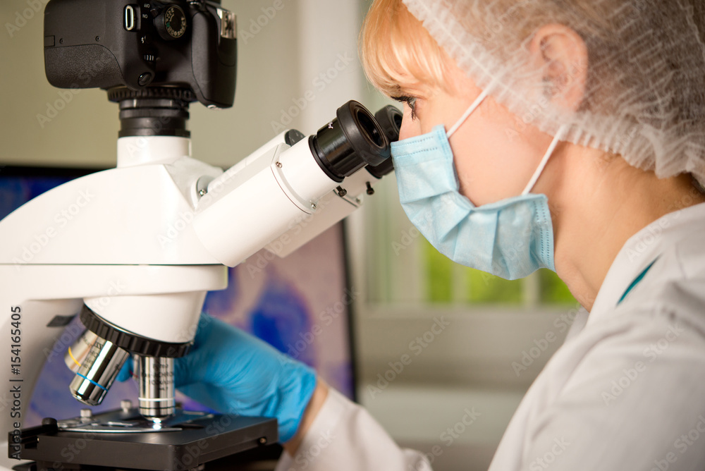 Laboratory assistant or technician in medical research lab looking into a microscope and doing research Laboratory assistant or technician in medical research lab looking into a microscope and doing research