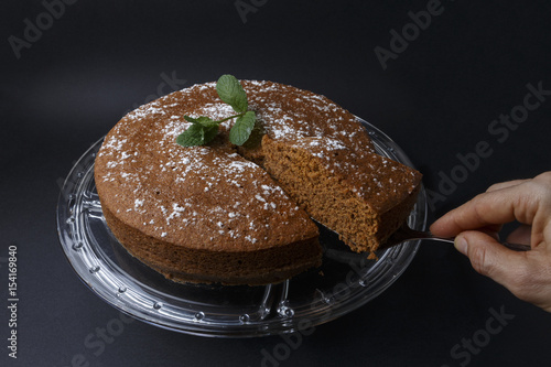 Woman serving a chocolate cake with sugar decoration with a spatula on glass stand 