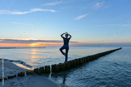 Frau macht Yoga im Sonnenuntergang am Meer