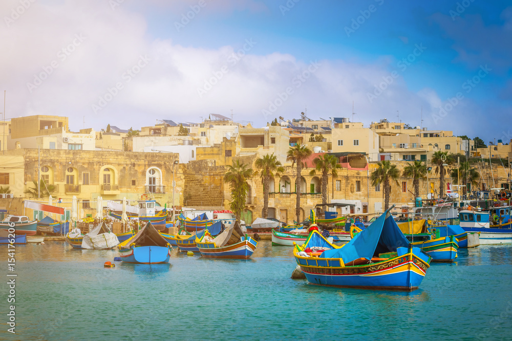 Marsaxlokk, Malta - Traditional colorful maltese Luzzu fisherboats at the old village of Marsaxlokk with turquoise sea water and palm trees on a summer day