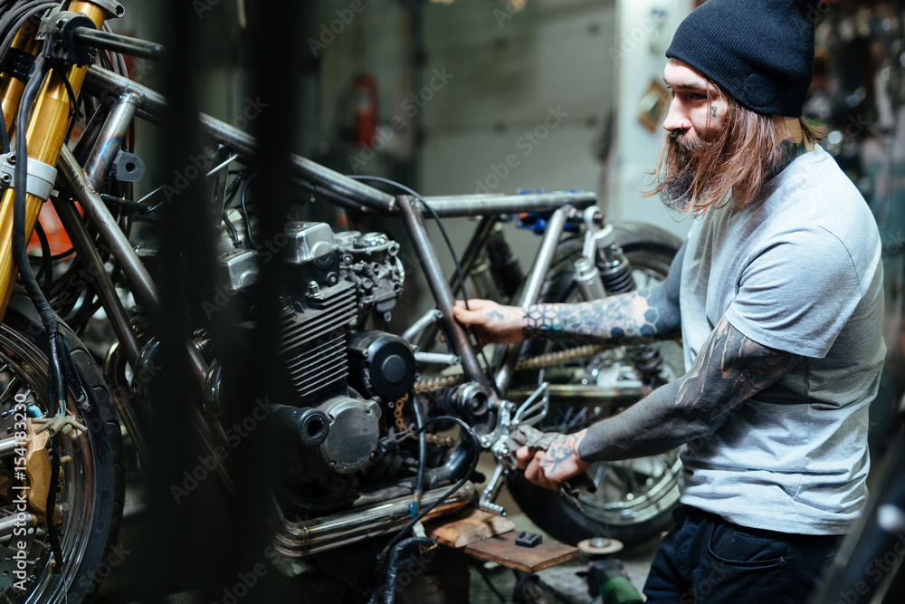 Fototapeta premium Hipster with tattoos repairing broken bikes