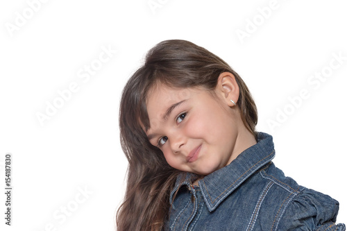Portrait of simper brunette long haired little girl isolated on the white background. The little girl is looking at a camera with a bowed head