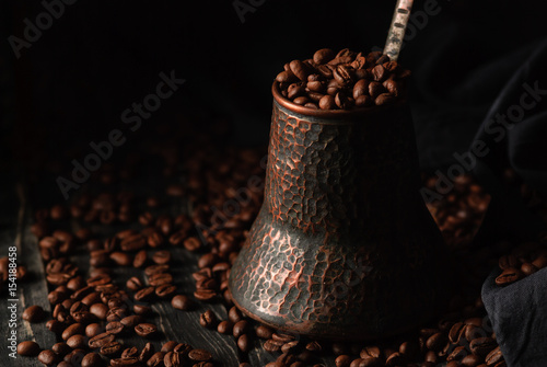 Coffee in grains in a copper turkish coffee pot on a wooden black table, black background. Close up, copy space photo