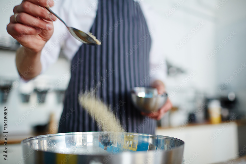 Baker adding salt in bowl with ingredients
