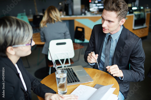 Portrait of young modern businessman talking to woman at table consulting client of banking products