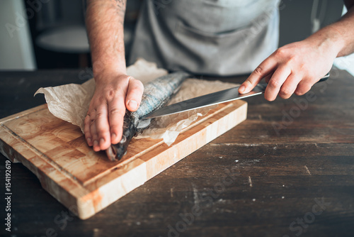 Billede på lærred Chef hands with knife cut up fish on cutting board