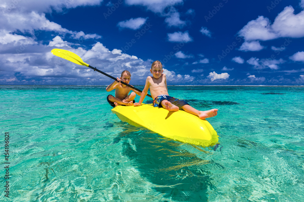 Two young caucasian boys kayaking at tropical sea on yellow kayak