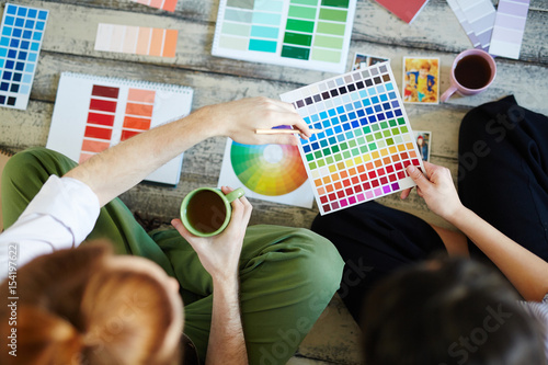 Directly above view of creative designers team discussing project, choosing color scheme laying out swatches on wooden floor