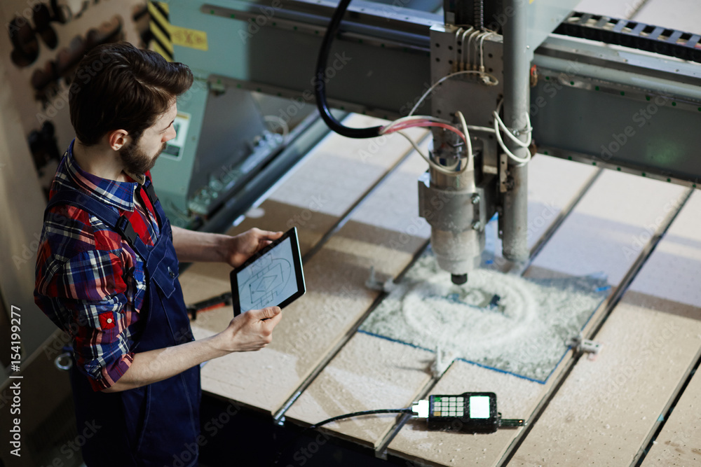 Factory worker operating cutter machine using digital tablet in workshop Factory worker operating cutter machine using digital tablet in workshop