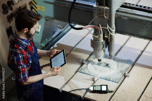Factory worker operating cutter machine using digital tablet in workshop