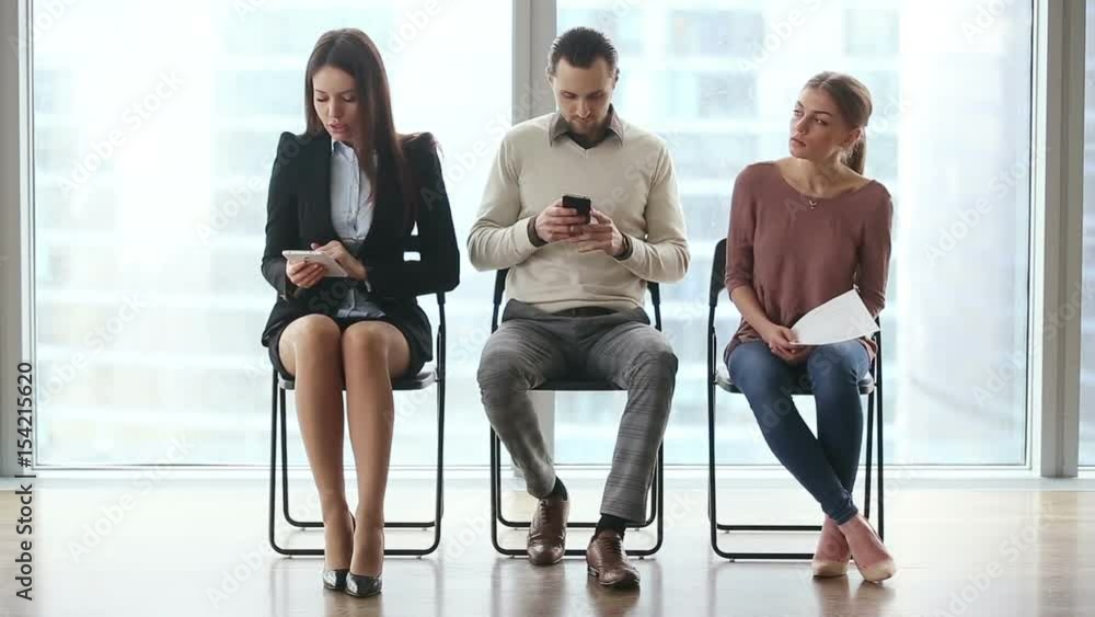Group of three young casual people candidates sitting on chairs in modern office lobby, waiting too long for job interview, using technology devices, feeling nervous. Full length. Job search concept Group of three young casual people candidates sitting on chairs in modern office lobby, waiting too long for job interview, using technology devices, feeling nervous. Full length. Job search concept