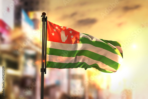 Abkhazia Flag Against City Blurred Background At Sunrise Backlight