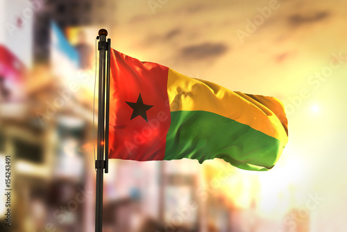 Guinea-Bissau Flag Against City Blurred Background At Sunrise Backlight
