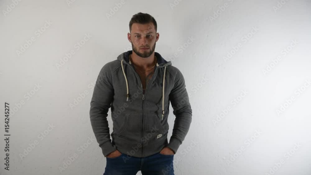 Bodybuilder handsome man undressing, taking off jacket against white background, revealing muscular naked torso in studio shot Bodybuilder handsome man undressing, taking off jacket against white background, revealing muscular naked torso in studio shot