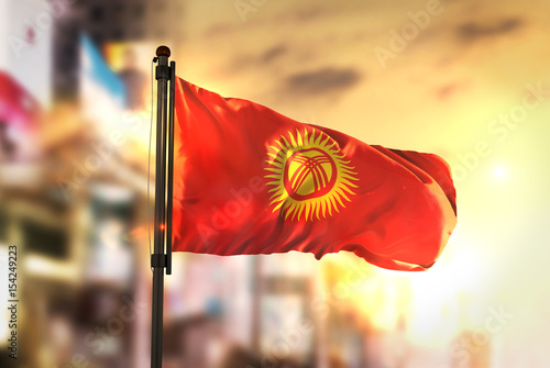 Kyrgyzstan Flag Against City Blurred Background At Sunrise Backlight