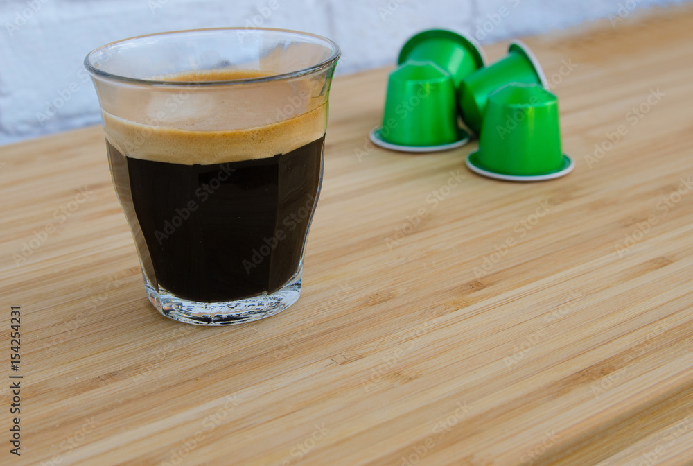 Close up of tasty espresso with foam and green coffee capsules on wooden background.Copy space. Close up of tasty espresso with foam and green coffee capsules on wooden background.Copy space.