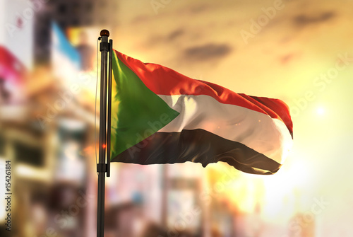 Sudan Flag Against City Blurred Background At Sunrise Backlight photo