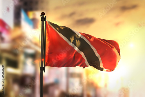 Trinidad and Tobago Flag Against City Blurred Background At Sunrise Backlight