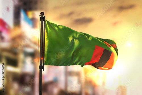 Zambia Flag Against City Blurred Background At Sunrise Backlight