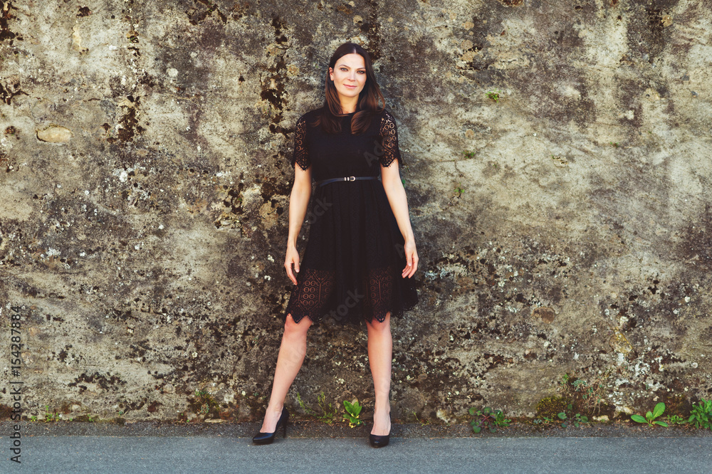 Fototapeta premium Outdoor portrait of young beautiful brunette woman wearing black lace dress and high heel shoes