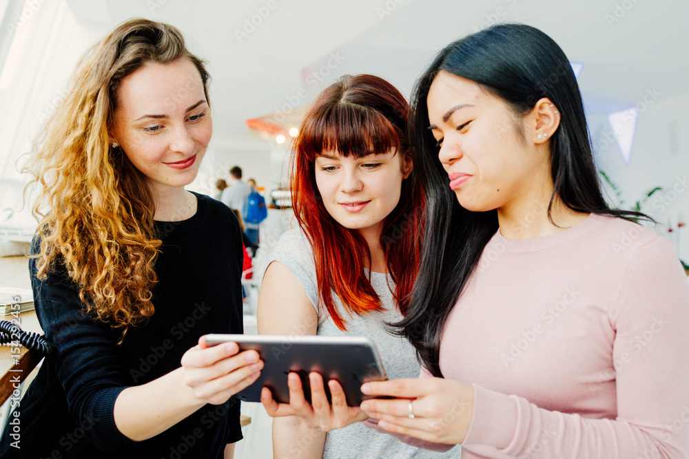 Three young girlfriends playing with a tablet while reviewing holyday photos Three young girlfriends playing with a tablet while reviewing holyday photos