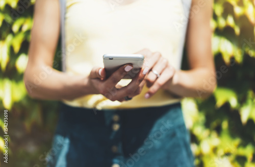 Hipster text message on smart phone or technology, mock up of blank screen. Young girl using cellphone on yellow flower background close. Tourist female hands holding gadget on blurred summer backdrop