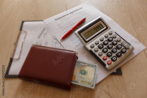 Close up view of the homeowner insurance policy. Insurance form with pen, notebook, dollars, calculator on the table