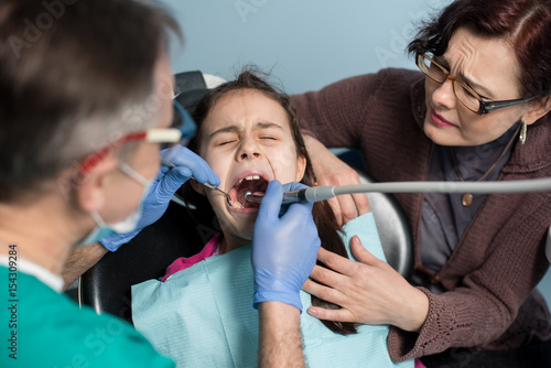 Young girl with her mother on the first dental visit. Senior pediatric dentist treating patient girl teeth at the dental office. Medicine  stomatology and health care concept. Dental equipment